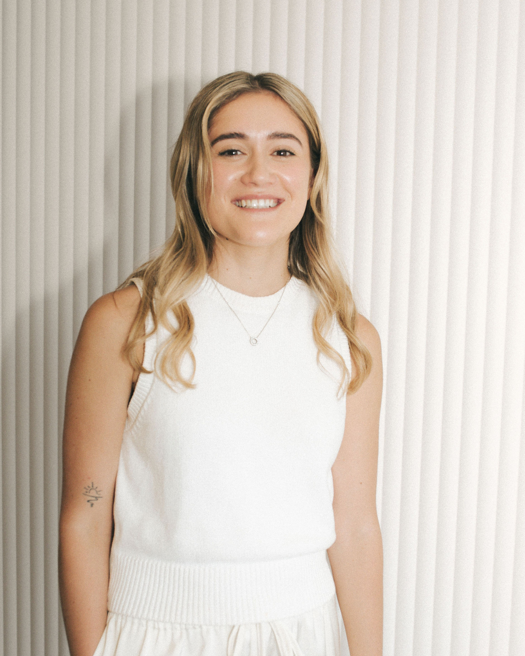 Woman wearing a white sleeveless top against a neutral background